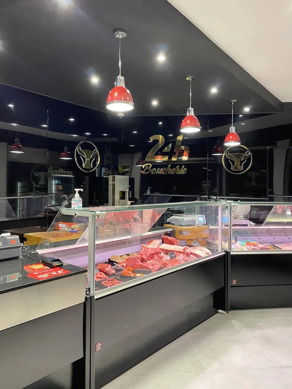 Le comptoir réfrigéré et les suspensions rouges de la boucherie, l'enseigne 24H au mur