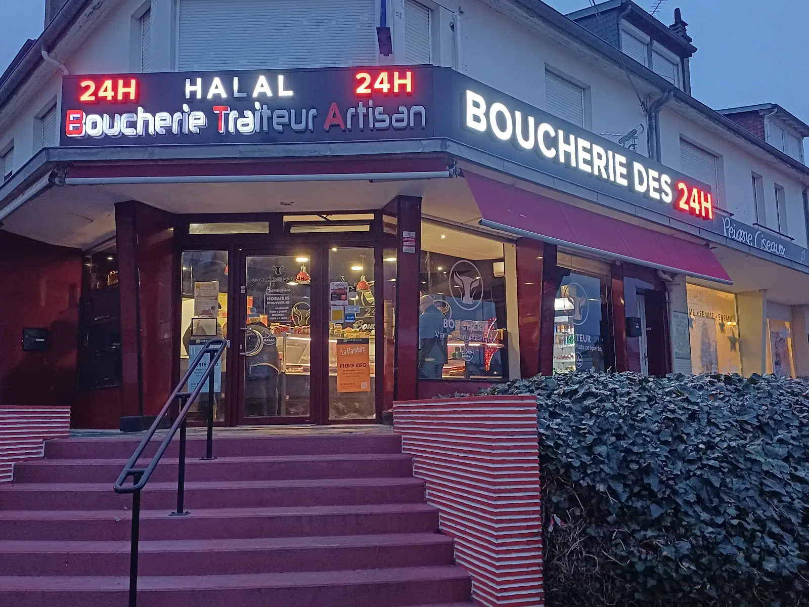 La façade de la Boucherie des 24H à la tombée du jour, l'enseigne allumée et l'escalier rouge